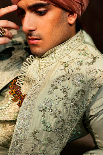 A pastel green waistcoat made from luxurious silk, intricately hand-embellished with Mughal floral patterns using matte sequins, tilla, resham, and cut dana thread-work. It is paired with a matching kurta and pajama set featuring a detailed floral neckline with an all-over motif, enhanced with sequins and resham embroidery.